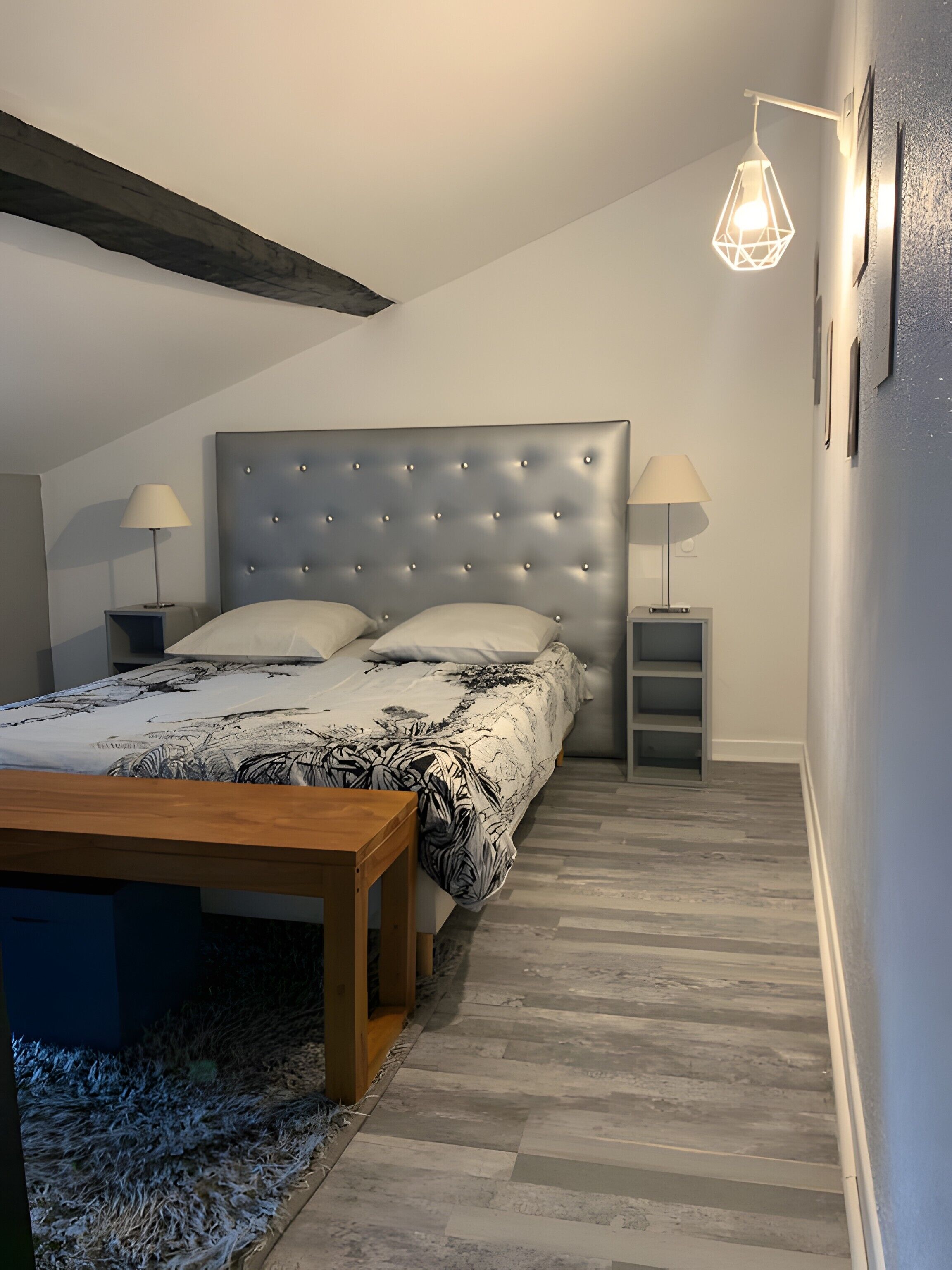 Une chambre à coucher comprenant un lit, des tables de chevet, une lampe, un banc en bois et un luminaire suspendu.