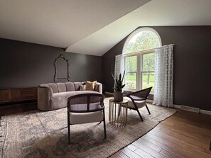 A room with a sofa, two chairs, a small table with a plant, and a large window with curtains.