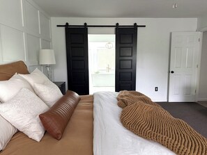 A bedroom with a bed, a nightstand, a lamp, a sliding door, and a white door.