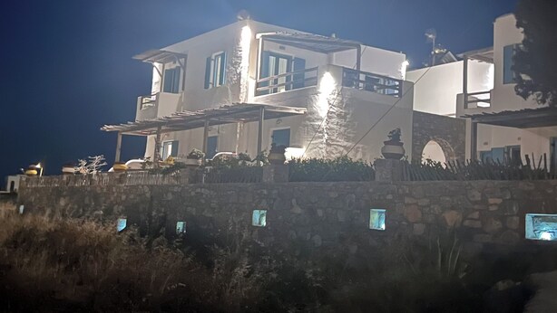 A large, multi-story building with a stone base and a flat roof, surrounded by vegetation. - Alexandras studios  (Irakleia)