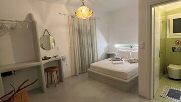 Camera da letto con un letto, una scrivania, una sedia, una lampada a sospensione e un bagno visibile attraverso una porta aperta.