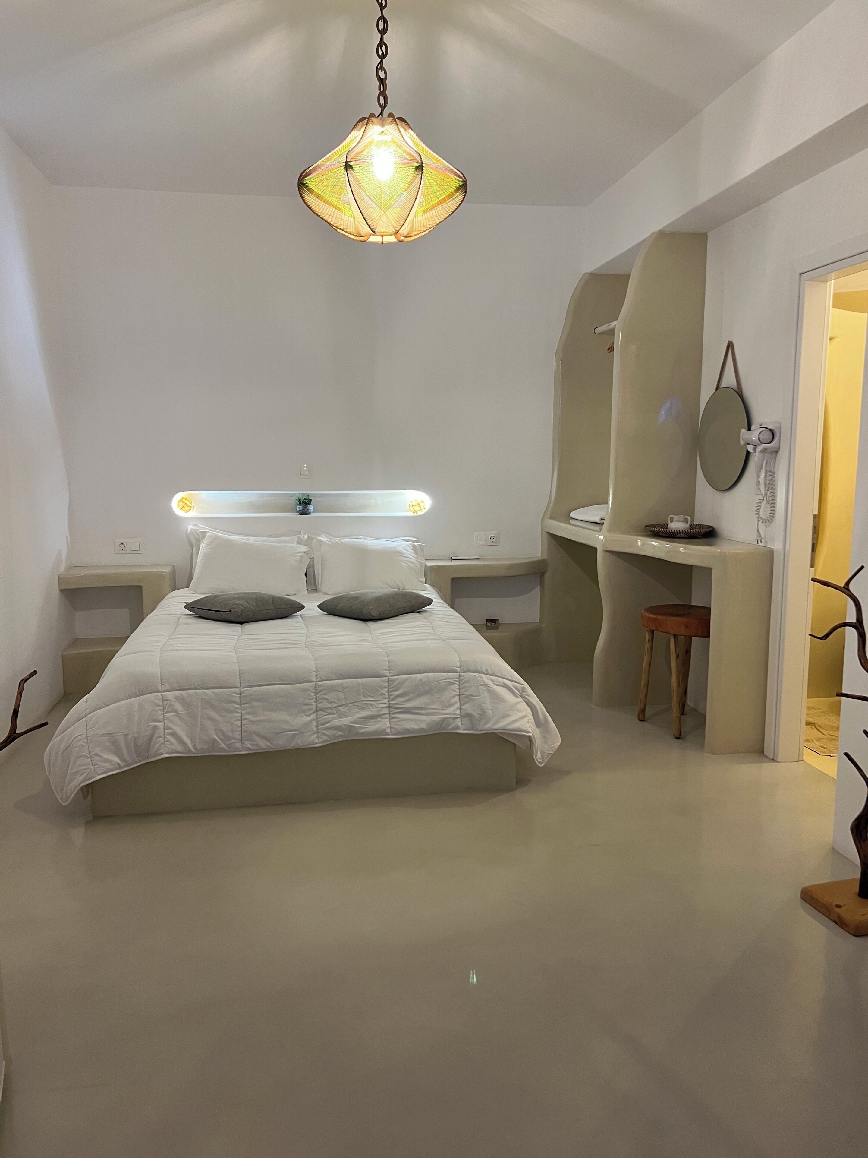 Un dormitorio con cama, mesitas de noche, escritorio, silla, lámpara colgante y espejo.