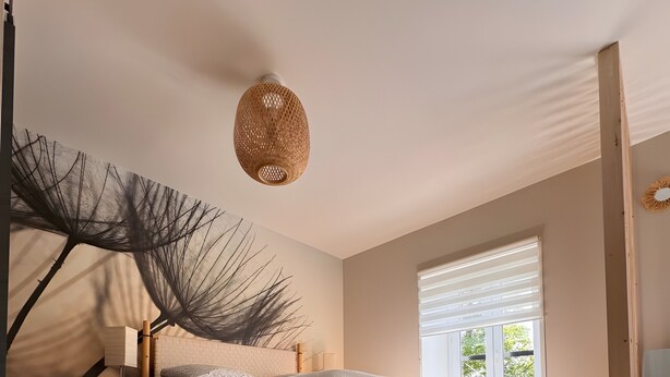 A bedroom with a bed, a hanging light fixture, a window with blinds, and a large wall art piece.