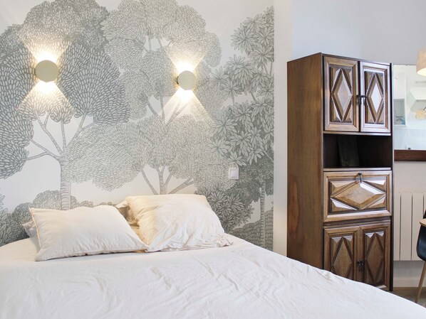 Ein Schlafzimmer mit einem Bett, einer Wand mit Baum-Wandgemälde und einem Holzschrank.