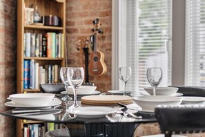 A dining table set with plates, glasses, and cutlery, with a guitar and bookshelves in the background. - Stylish 2Bed Flat Near Hampton Court & RiverThames - Pass the Keys (East Molesey)