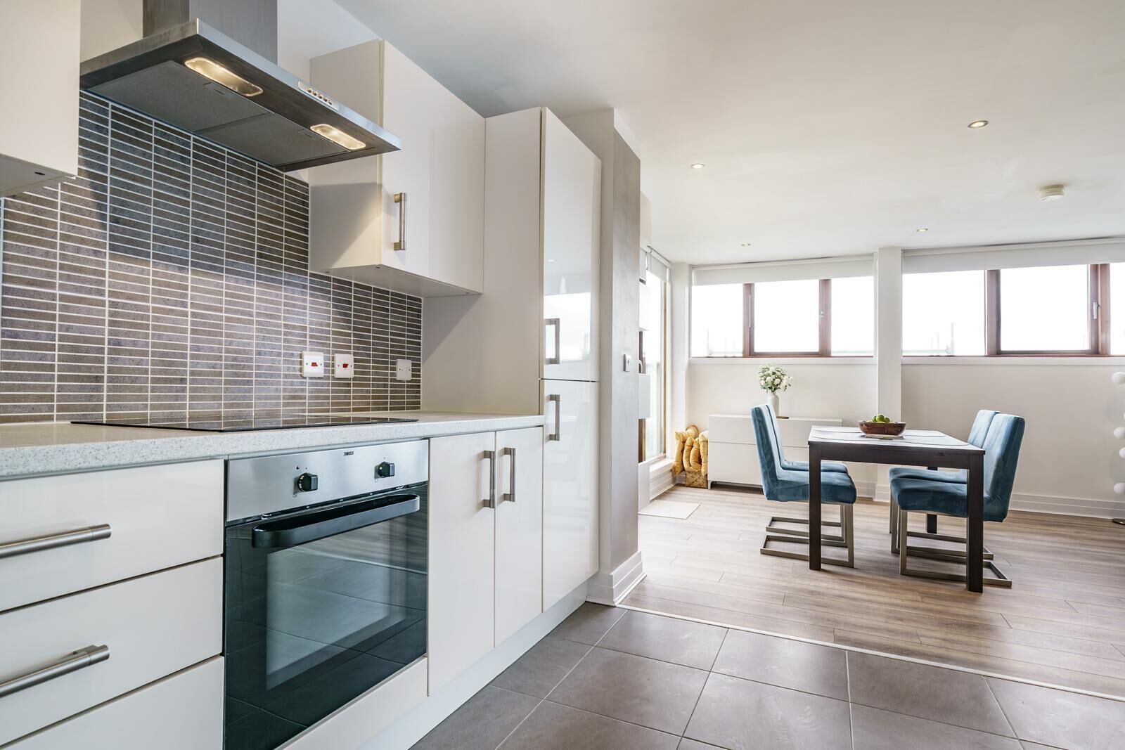A modern kitchen with a built-in oven, white cabinetry, and a dining area with a table and chairs.