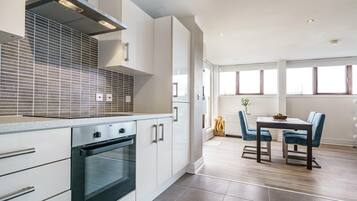 A modern kitchen with a built-in oven, white cabinetry, and a dining area with a table and chairs.