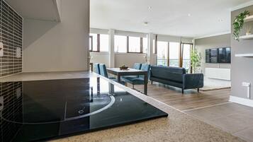 A modern kitchen with a black countertop, a dining area with a table and chairs, a sofa, and a TV mounted on the wall.