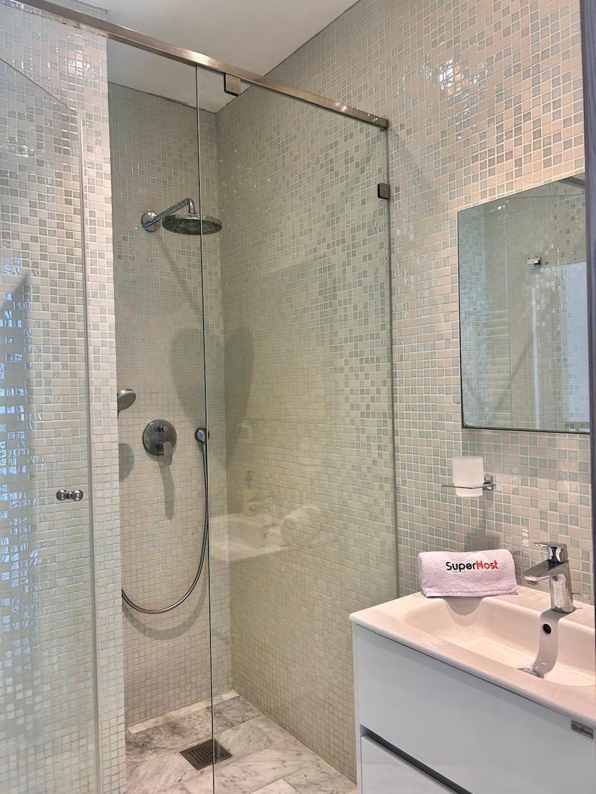 A glass-enclosed shower with a handheld showerhead, a wall-mounted faucet, and a tiled floor.