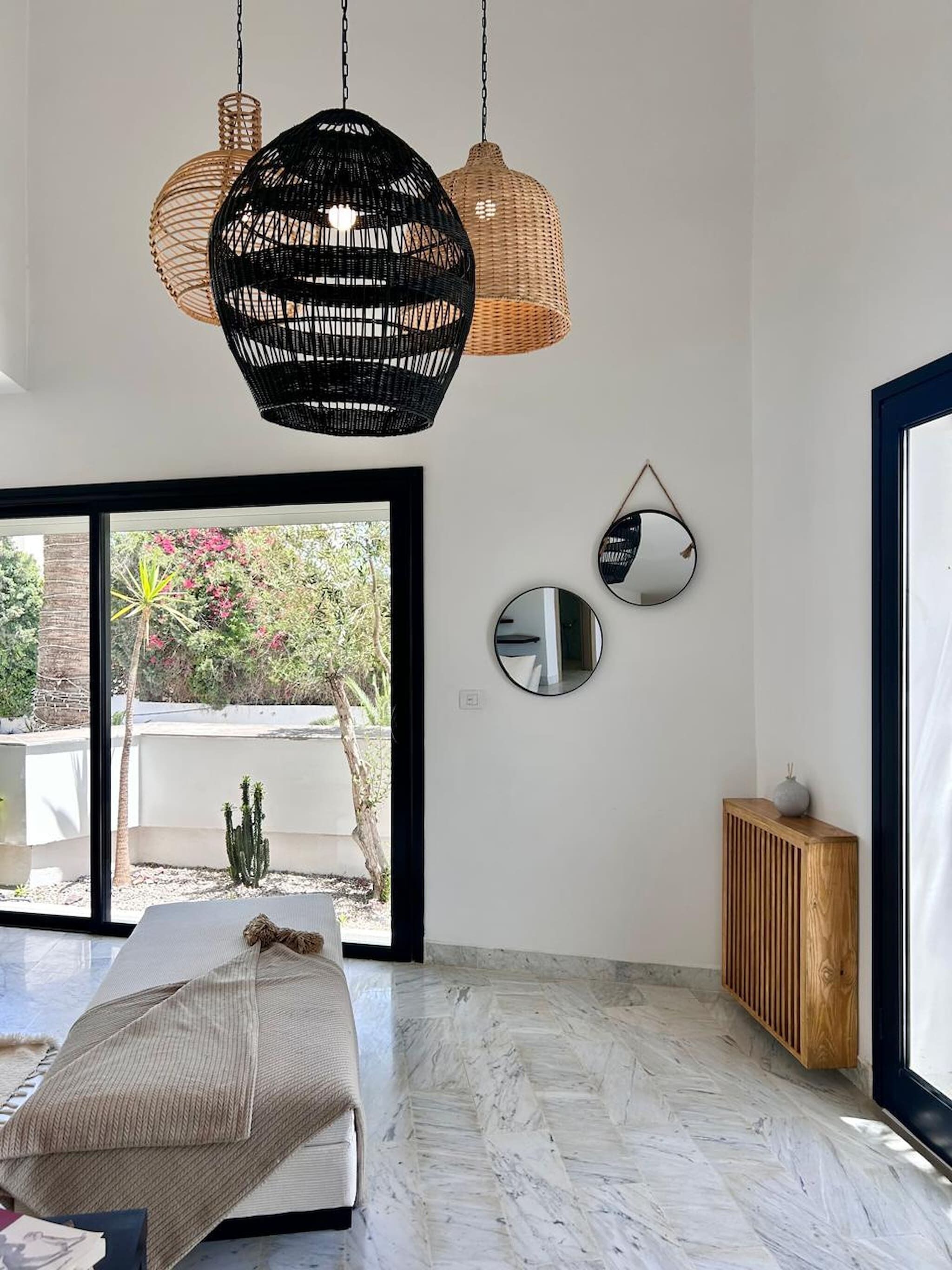 A bedroom with a bed, a large window, a hanging light fixture, and a wooden console.