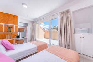 Ein Schlafzimmer mit zwei Betten, einem Holzschrank, einem Regal mit Körben und Blick auf die Stadt durch ein großes Fenster.