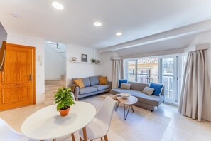 Ein modernes Wohnzimmer mit einer Couch, einem Esstisch mit Stühlen, einer Treppe und einem großen Fenster mit Vorhängen.