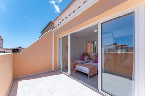 Ein Balkon mit Glastür, der zu einem Schlafzimmer mit zwei Betten und einem kleinen Tisch führt.