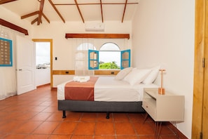A bedroom with a bed, bedside table, and a window with open shutters. - HOTEL CROSSMAN (Puerto Ayora)