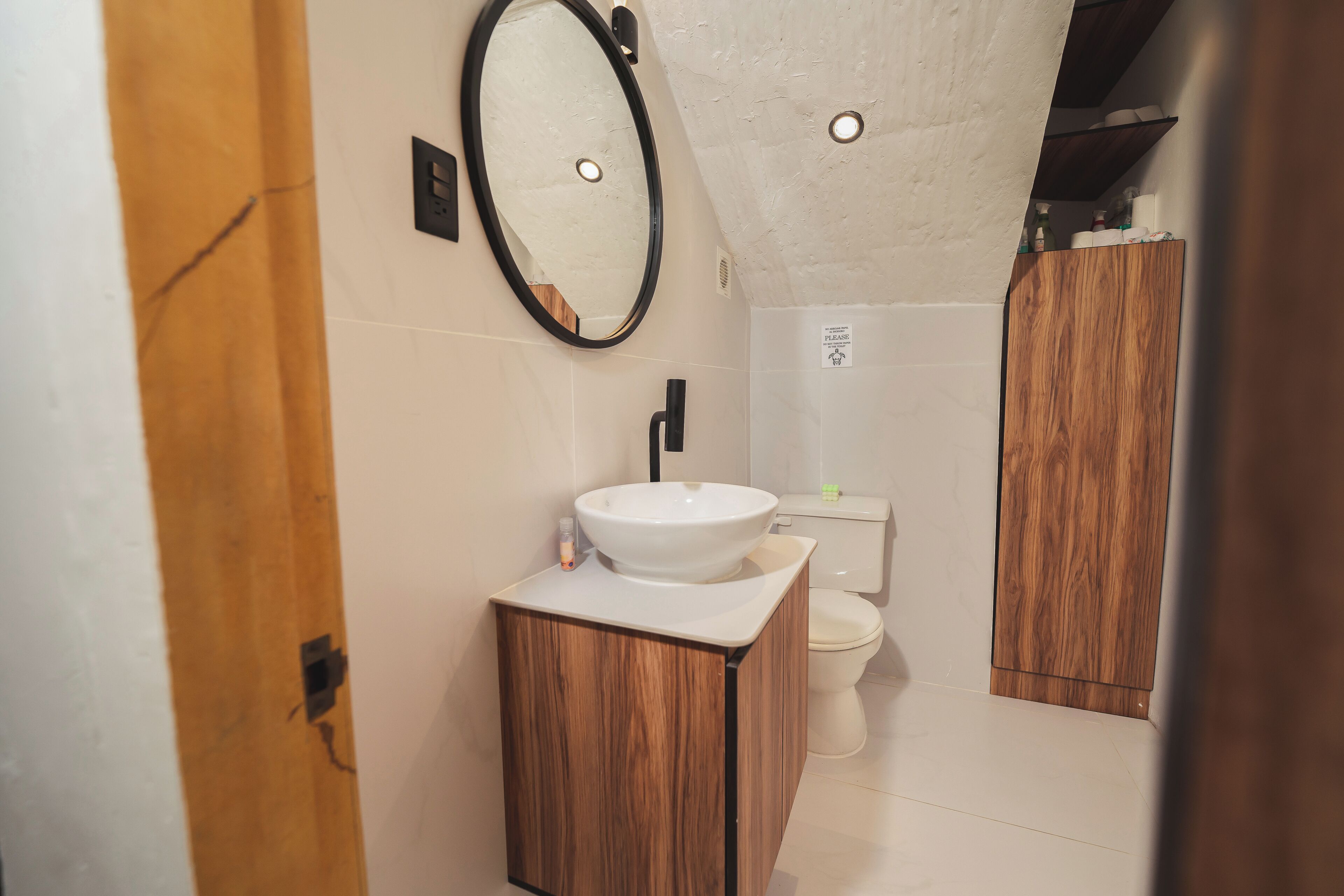 Un baño moderno con tocador de madera, lavamanos blanco, espejo y retrete.