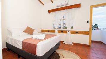 Habitación de hotel con cama, ventana con cortinas, vista al exterior y ventilador de techo.