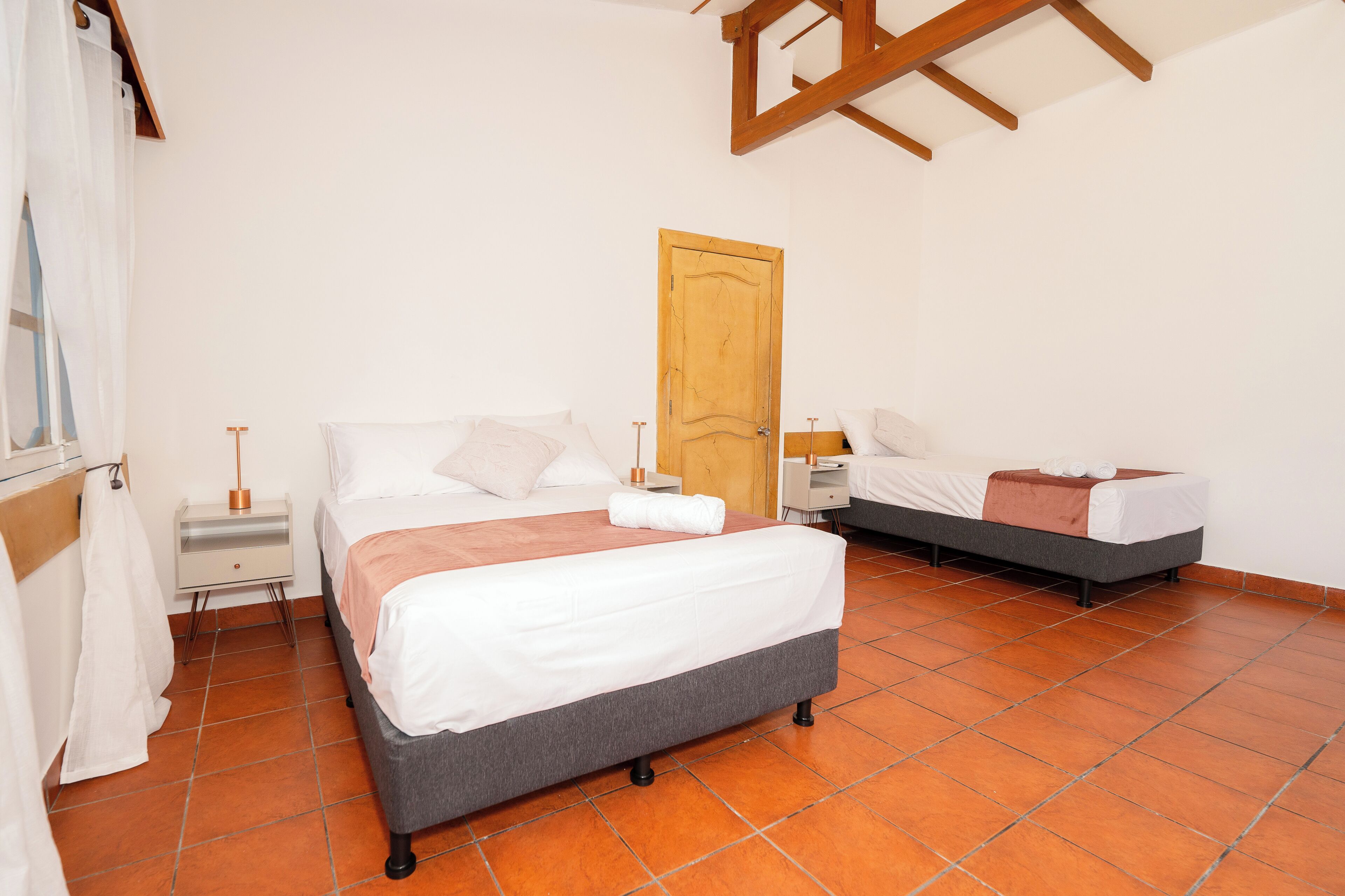 A bedroom with a large bed, a smaller bed, a wooden door, and a nightstand with a lamp.