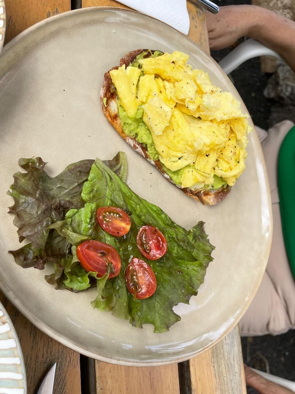 A plate with scrambled eggs, avocado, and cherry tomatoes on a bed of lettuce.