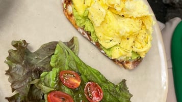 A plate with scrambled eggs, avocado, and cherry tomatoes on a bed of lettuce.