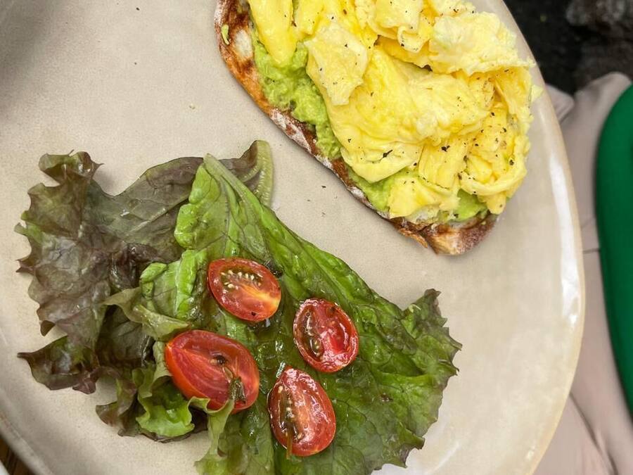 A plate with scrambled eggs, avocado, and cherry tomatoes on a bed of lettuce.