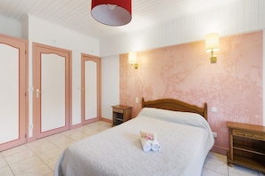 Une chambre à coucher comprenant un lit, deux tables de chevet, une petite table en bois, une lampe fixée au mur et une porte avec une poignée.