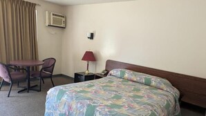 A hotel room with a bed, a desk, a chair, a lamp, and an air conditioning unit. - Algonquin Motor Lodge (Edmonton)
