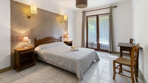 Ein Schlafzimmer mit einem Bett, Nachttischlampen, einem Holznachttisch, einem Sessel, einem Tisch und einem großen Fenster mit Vorhängen.