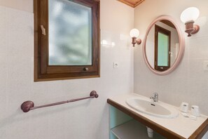 A bathroom with a wooden-framed window, a round mirror with wall-mounted lights, a white sink, and a grab bar. - Guest Room 4 with Pool (Saint-Pompont)