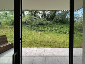 Blick aus einem Zimmer mit Schiebeglastür auf einen begrünten Garten mit üppigem Strauchwerk.