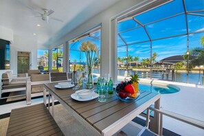 Un área de comedor con vistas a una piscina y palmeras.