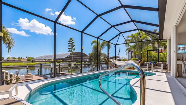 An indoor swimming pool with a view of a lake and buildings in the background. - Heated Pool, Gulf Access & Waterfront Luxury Escape - Seaside Social - Roelens (Cape Coral)