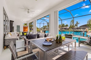 Ein moderner Innenraum mit Blick auf einen Pool, einem Essbereich mit Tisch für zwei Personen und einer Sitzecke mit einer Couch und Sesseln.