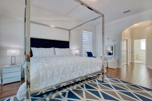 Ein Schlafzimmer mit Himmelbett, Nachttisch, Spiegel, Kommode und einem durchgegangene Tür erkennbaren Badezimmer.
