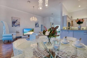 Una sala de estar moderna con una mesa de comedor de vidrio, sofás blancos, un televisor y obras de arte en las paredes.