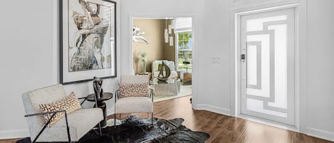 A modern living room with a large abstract painting, two patterned armchairs, a coffee table, and a black leather rug.