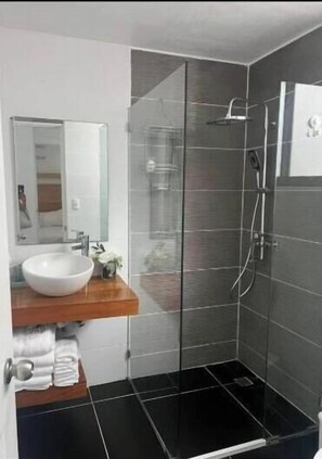 Ein modernes Badezimmer mit einer Duschkabine aus Glas, einem weißen Waschbecken und einem Badezimmermöbel aus Holz.