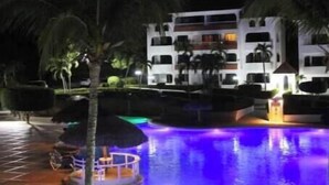 A swimming pool with a water feature, palm trees, and a multi-story building in the background. - 1 bedroom and 1 bathroom apartment in Monte Vista, Sosúa (Sosúa)