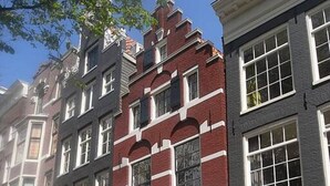 A row of traditional European-style buildings with distinct architectural features, including red brick facades, white window frames, and a central staircase leading to the entrance. - Sonnenberg - Canal side & view - Private & Central (Amsterdam)