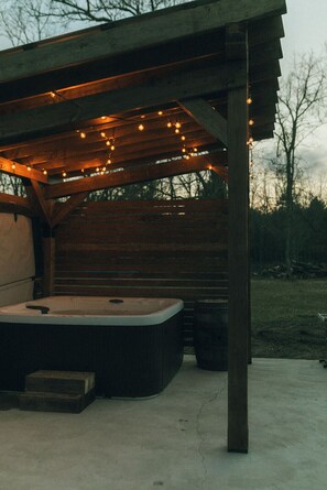 A wooden structure with a hot tub under a pergola, string lights, and a concrete floor. - Irons Legend's Acres Hot Tub, Fire Pit Near Trails (Irons)