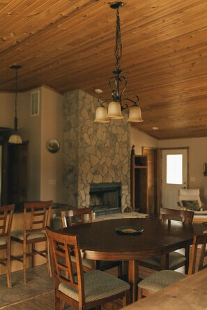 A wooden dining table with chairs, a stone fireplace, and a hanging light fixture. - Irons Legend's Acres Hot Tub, Fire Pit Near Trails (Irons)