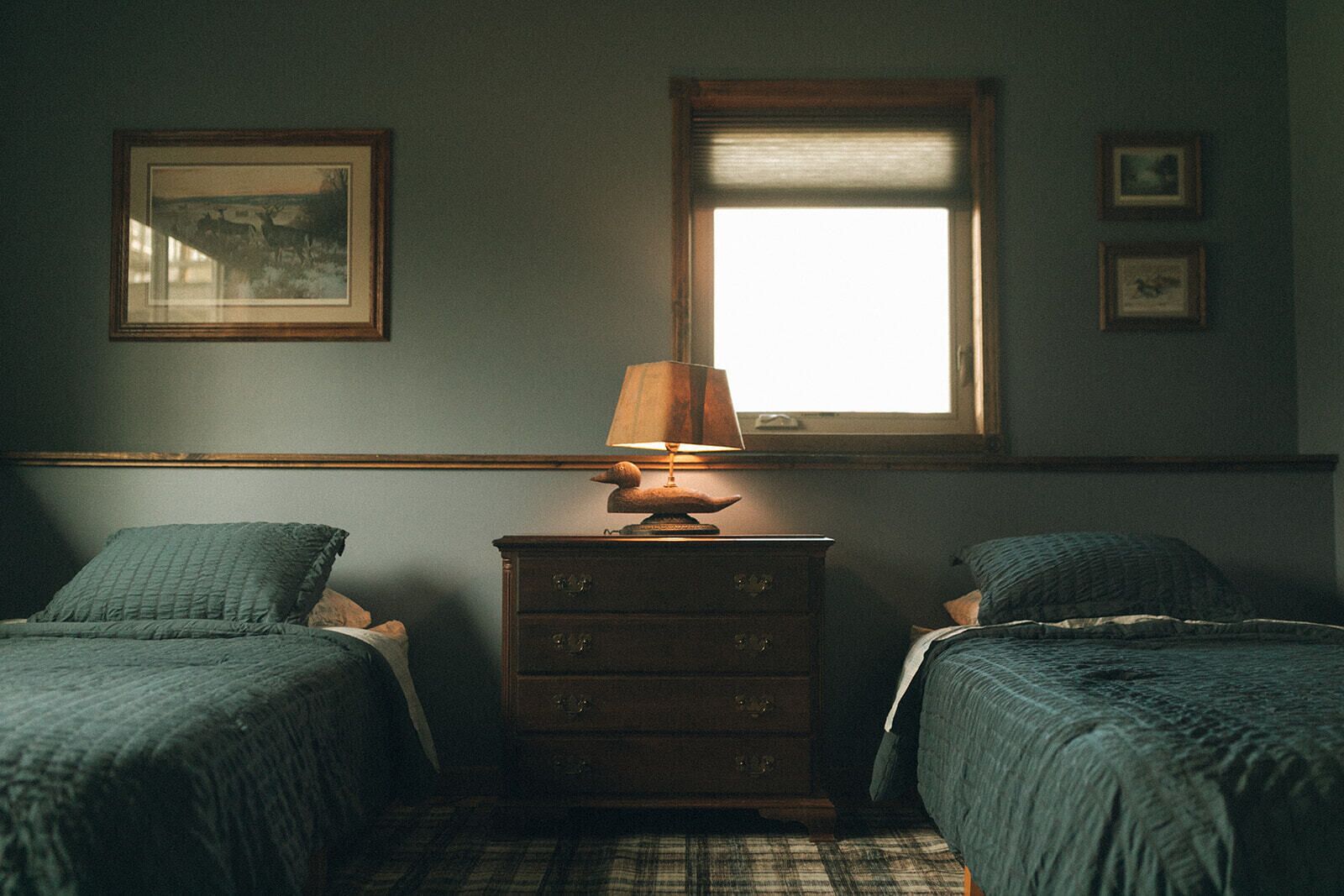 Un dormitorio con dos camas, una mesita de noche, una lámpara y una ventana con persianas.