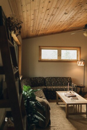 A room with a wooden ceiling, a window, a sofa, a table, and a floor lamp. - Irons Legend's Acres Hot Tub, Fire Pit Near Trails (Irons)