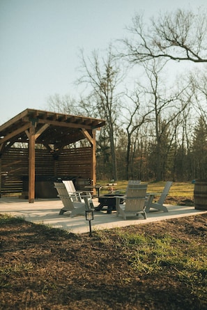 Een houten blokhut met een overdekt terras, zitplaatsen buiten en een vuurkorf.