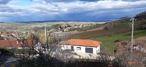 Ländliche Landschaft mit einem weißen Gebäude und rotem Dach, umgeben von viel Grün und einer in der Ferne liegenden Stadt.