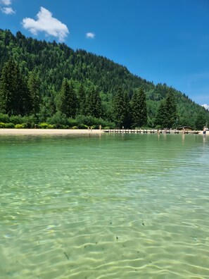 A clear lake with a forested hillside in the background.