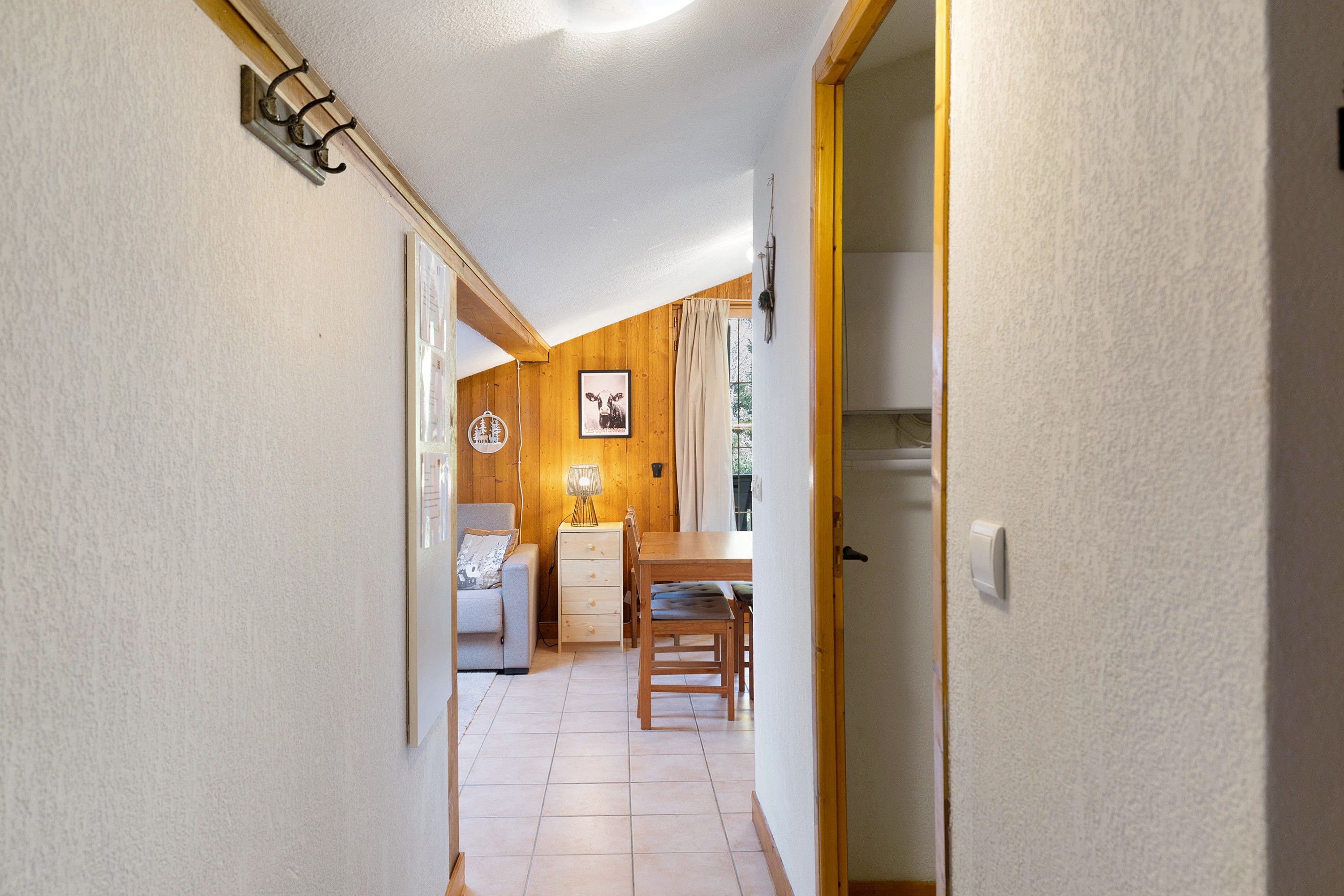 A narrow hallway leading to a dining area with a wooden table and chairs, a lamp, and a framed picture on the wall.