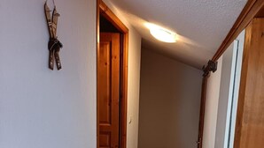 Un pasillo estrecho con puertas de madera, suelo de baldosas y un aplique en el techo.