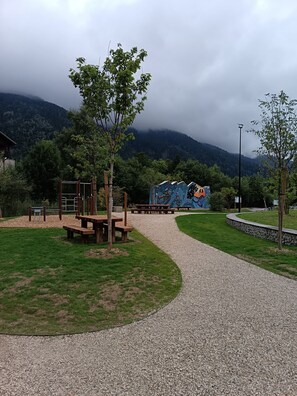 Un parque infantil con un área de escalada, mesas de picnic y un mural de fondo.
