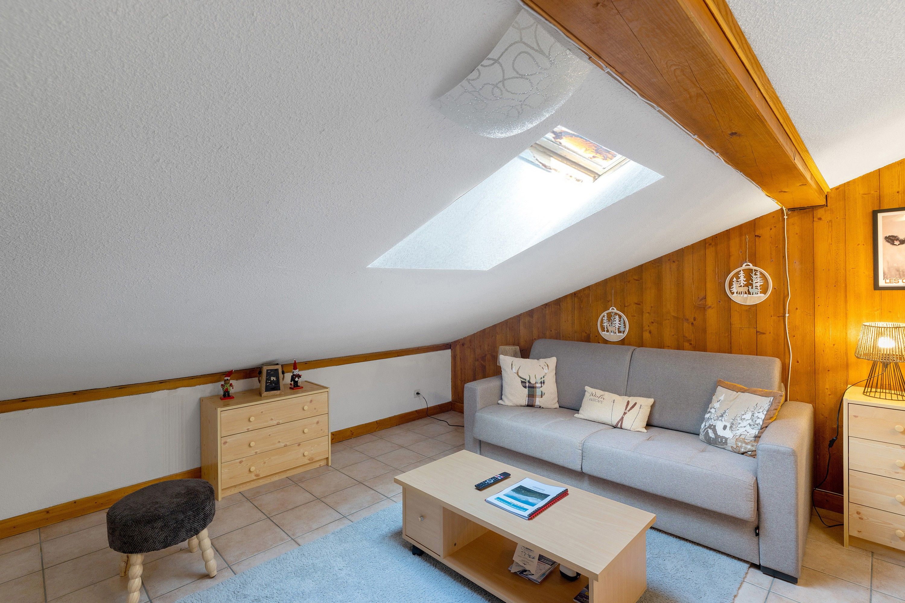 Une chambre mansardée chaleureuse, avec un plafond en pente, un canapé, une petite table, une commode en bois et une lucarne.