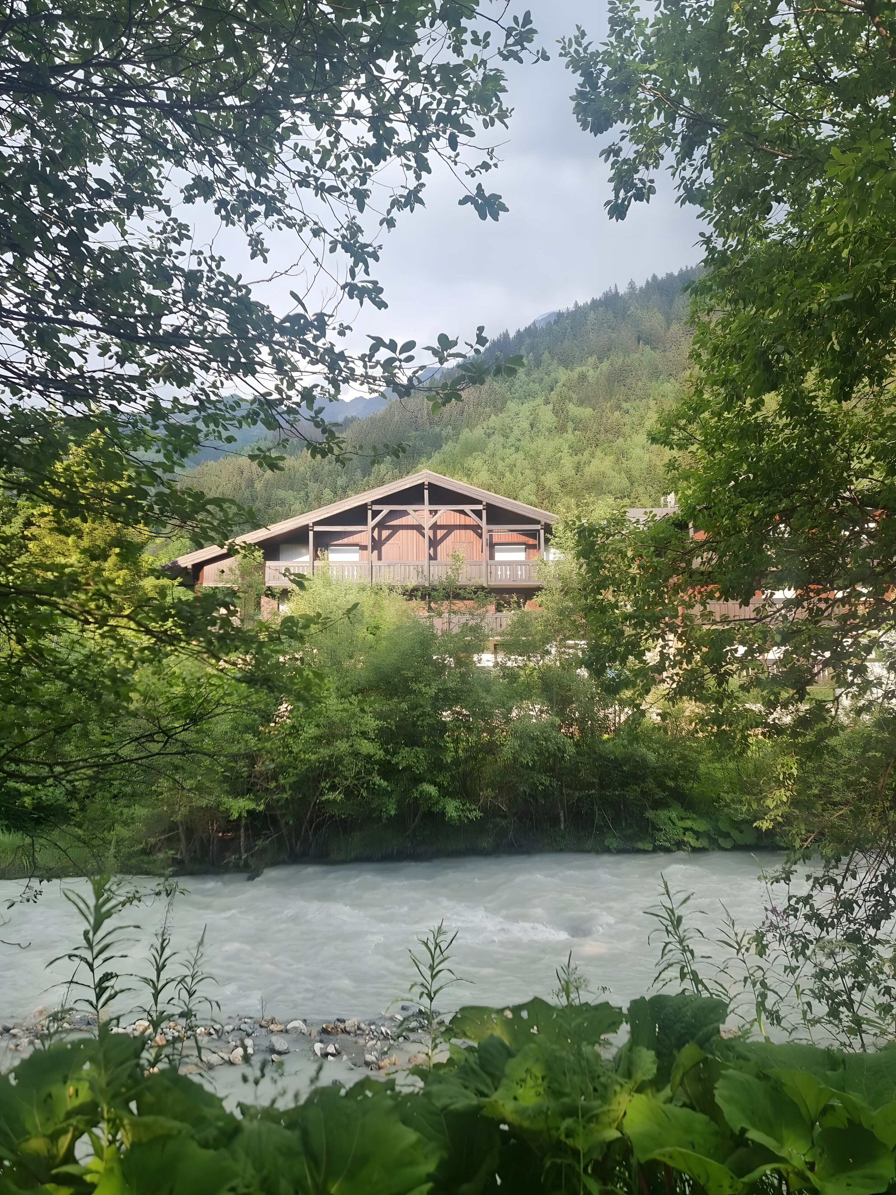 Eine Holzhütte mit Balkon, umgeben von dichtem Grün und einem Fluss.